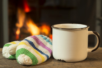 Hot drink and children's  knitted gloves to warm and positive mood on the background of a blazing fire in the oven / After playing in the snow