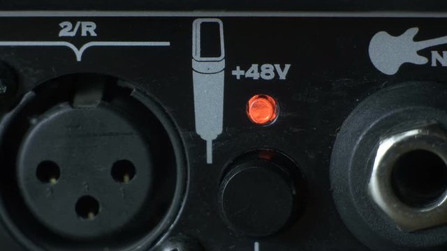 Close-up male finger pressing switchable 48V phantom power on black Audio Interface. Phantom power supply.