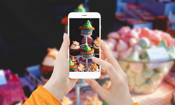Girl taking picture with phone of cupcakes on stand