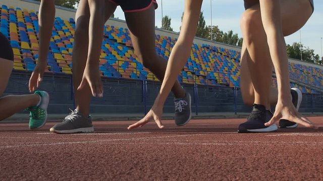 Close-up of young female athletes preparing to run at starting line, slow-motion