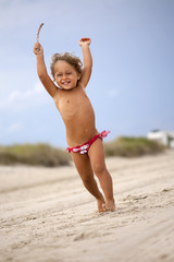 Jumping Baby Girl on the beach with a stick