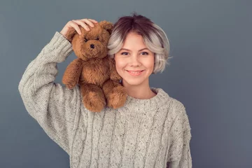 Fotobehang Young woman in a woolen sweater isolated on grey wall winter concept holding teddy bear © Viktoriia