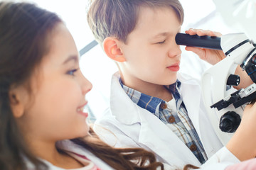 Little kids learning chemistry in school laboratory looking in a microscope close-up