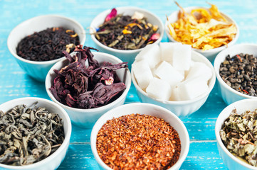 Various dried medicinal herbs and teas in several bowls on blue wooden background