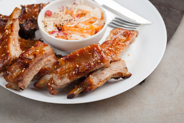 Grilled pork ribs in barbecue sauce and honey with sauerkraut on white plate. Snack to beer on a light stone table