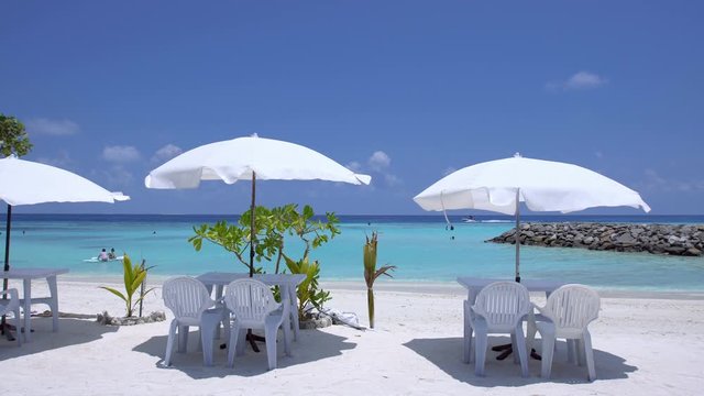 White sun umbrellas with tables and chairs at sandy beach