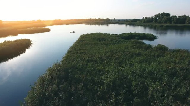 A wonderful view of the Dnipro river inflows and islets covered with patches of sedge, cane, lily and reed at a sparkling sunset in summer