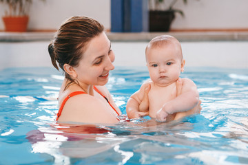 White Caucasian mother traning her newborn baby to float in swimming pool. Baby diving in water. Healthy active lifestyle. Family activity and early development concept