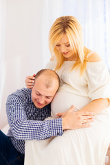 Fototapeta na wymiar A man in a stylish shirt sits next to his pregnant wife and puts