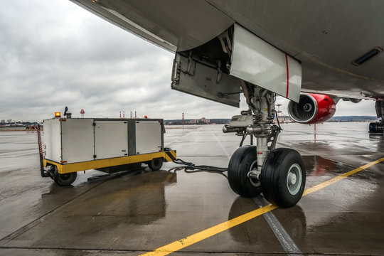 Close-up view on front landing gear of large passenger civil aircraft and ground power unit near of it
