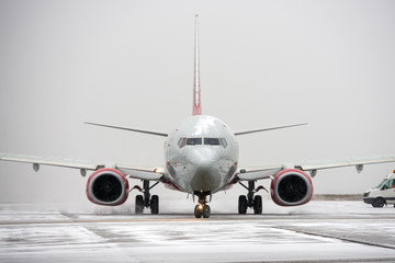 Modern twin-engine passenger airplane taxiing for take off at airport during snow blizzard