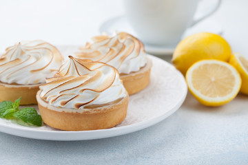 Lemon tartlets with meringue on vintage white plate and Cup of tea on the stone table. Tasty treat on a light blue background
