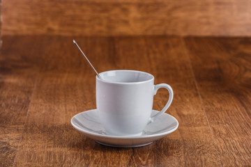 white coffe Cup with spoon on white saucer on dark brown wooden background