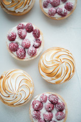 Delicious lemon and raspberry tartlets with meringue on a white vintage plate. Sweet treat on a light blue background. Flat lay and copy space. Top view