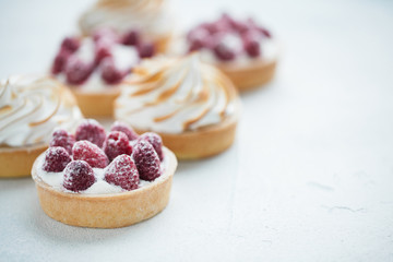 Delicious lemon and raspberry tartlets with meringue on a white vintage plate. Sweet treat on a...