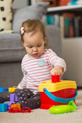 Two years old toddler girl playing on the floor, putting plastic shapes into the box with appropriate holes, focus on the toy