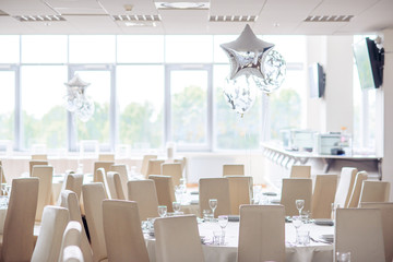 Serving a festive round table decorated with white elegant chairs and decorated with balloons for a festive dinner.