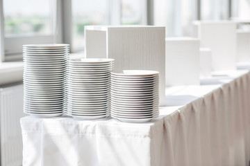 Stack of white ceramic plates on the white long table. Preparing for festive dinner and serving the table.