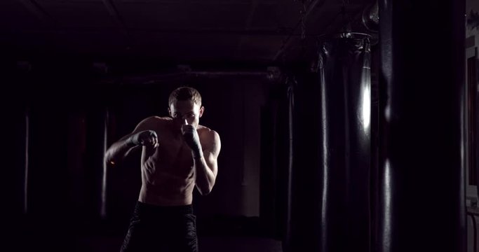 Kickboxer shadow boxing as exercise for the fight. Fighter training punching. Boxing in the darknes. Young boxer training in the gym