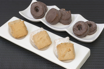 Dos platos con pasteles y pastas variados sobre 
un mantel negro