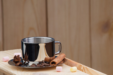 A cup of coffee on a wooden shelf, with cinnamon, anise, coffee beans and marshmallow.