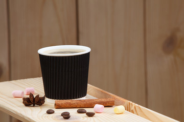 A cup of coffee on a wooden shelf, with cinnamon, anise, coffee beans and marshmallow.
