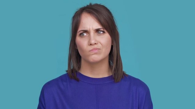 Portrait of serious young female expressing displeasure or disinterest with facial expressions meaning not good over blue background. Concept of emotions