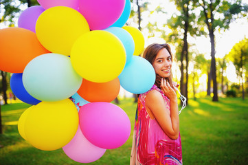 Beautiful, cheerful young woman in a bright dress with colorful balloons  on a field with a blue...