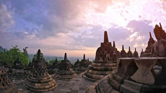 Scenic panoramic view of Borobudur temple at sunrise with beautiful sky and Buddha stone sculpture in meditation pose sitting in buddhist stupa. Traveling to Java Indonesia