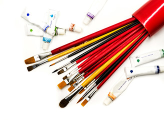 set of bright red paintbrushes and watercolor tubes scattered on the white background