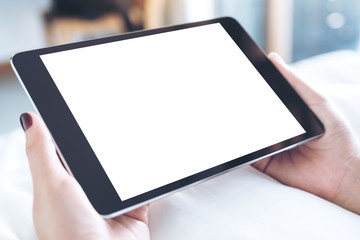 Mockup image of woman's hands holding black tablet pc with blank desktop white screen while sitting on a white bed