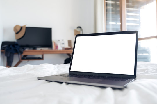 Mockup image of laptop with blank white desktop screen on the bed in bedroom