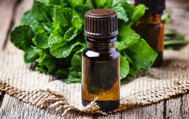 Essential oil of peppermint in a small brown bottle with fresh green mint, rustic style, vintage wooden background, selective focus