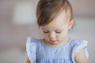 Naklejka premium Portrait of a cute little baby girl in a blue dress looks down