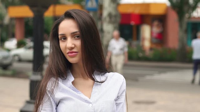 Portrait of beautiful girl with long dark hair in the city, in the background blurred people.