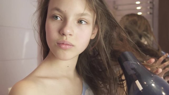 Beautiful teen girl dries hair a hairdryer in bathroom stock footage video