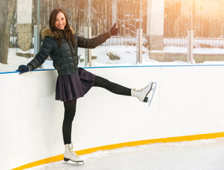 The girl on the skates and on the ice by the boards and posing