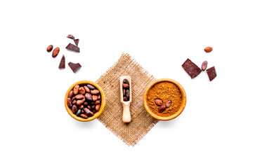 Chocolate and cacao concept. Cocoa powder in bowl near cocoa beans and broken chocolate on white background top view copy space