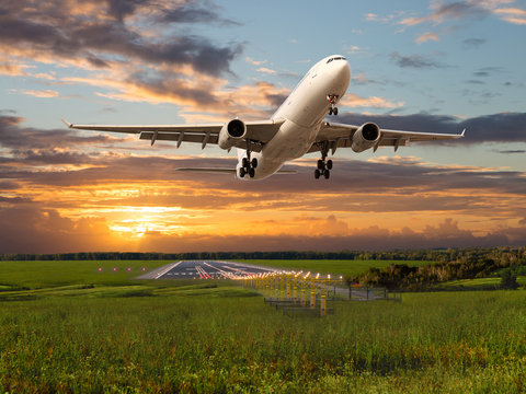 Passenger plane takes off from the airport runway during the sunset.
