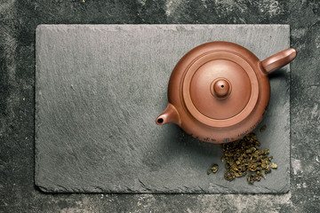 Brown ceramic teapot on black stone tray, top view.