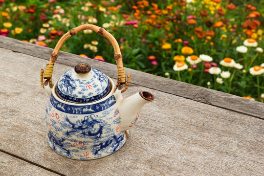 Chinese teapot with green tea on a wooden table on a background of bright colorful flowers, top view. Pai, Thailand.