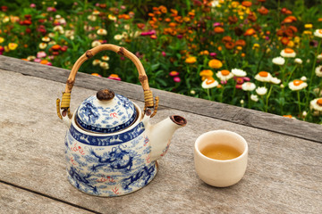 Chinese teapot and cup with green tea on a wooden table on a background of bright colorful flowers,...