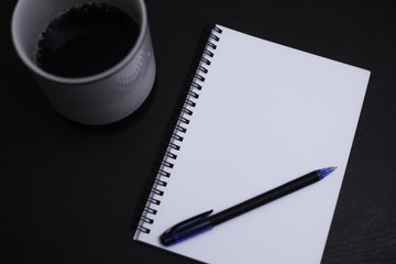 Notebook and black coffee on wood background.
