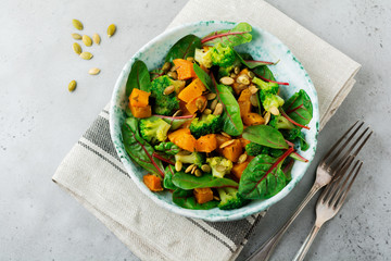 Salad with a baked pumpkin, chard, broccoli, and pumpkin seeds in ceramic plate on stone or concrete background table background. Selective focus. Rustic style. Top view. Copy space.