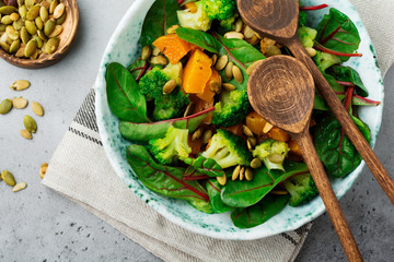 Salad with a baked pumpkin, chard, broccoli, and pumpkin seeds in ceramic plate on stone or concrete background table background. Selective focus. Rustic style. Top view. Copy space.