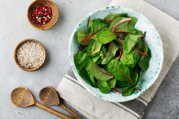 Fresh young leaves of chard for salad in a dark ceramic dish on gray concrete background. Selective focus. Copy space. Top view.