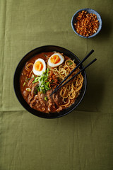 Japanese ramen with pork belly, mushrooms and marinated eggs on green linen tablecloth. Top view