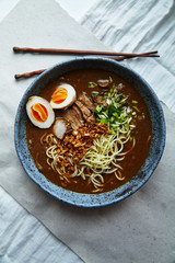 Japanese ramen with pork belly, mushrooms and marinated eggs served in blue handmade ceramic bowl garnished with chives