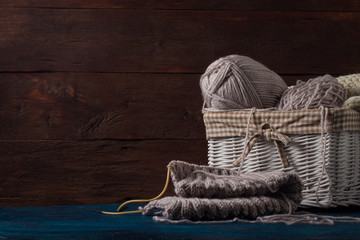 Light gray Knitting in a basket and knitting needles, a white knitted scarf on a wooden background. The concept of handmade