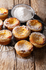 Homemade pastries: delicious pastel de nata with custard, sprinkled with powdered sugar close-up on the table. vertical